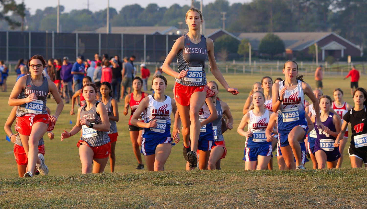The varsity girls field tops a hillock at the start of the race, led by Olivia Hughes of Mineola, her teammates, as well as the Quitman girls, who went on to win the meet.